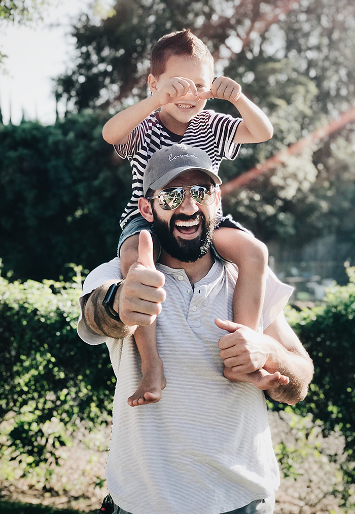 Man smiling and giving thumbs-up with child on shoulders